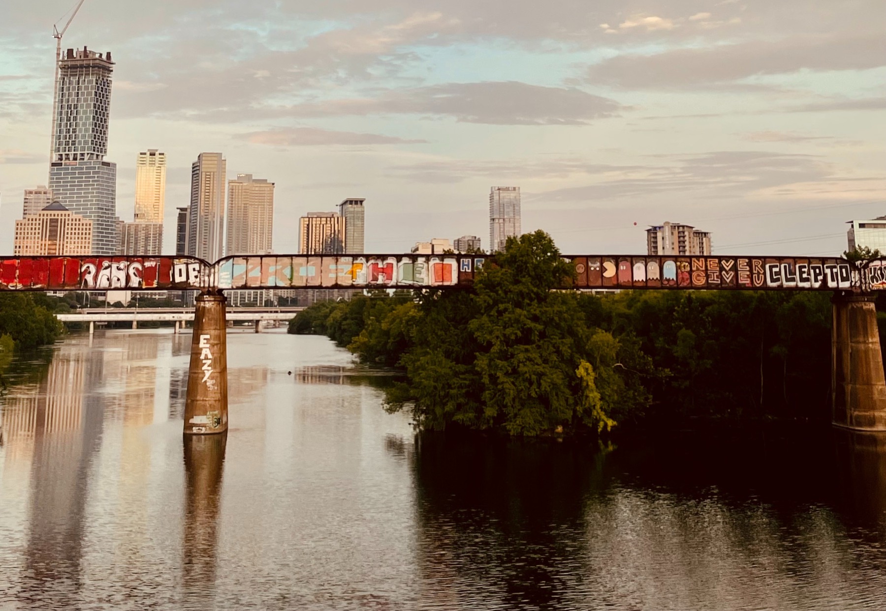 The downtown Austin skyline at sunset behind the graffiti-covered railroad trestle over Lady Bird Lake