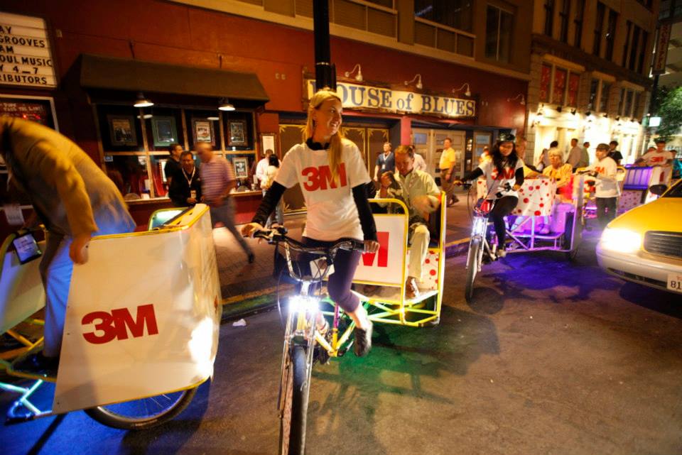 Drivers in 3M branded shirts riding lit carriages past the House of Blues at night