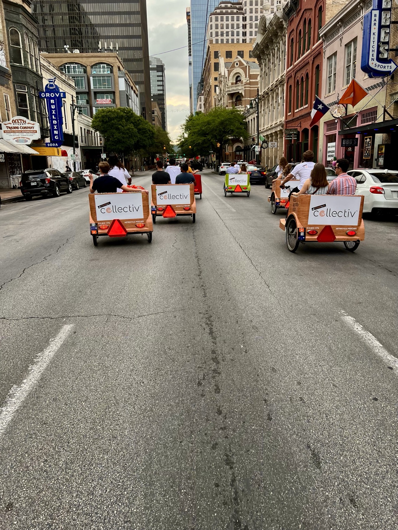 A line of Pedicab Adventures pedicabs carrying passengers down East Sixth Street in downtown Austin at dusk, each carriage carrying a branded ad panel