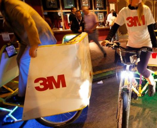 A rider in a 3M branded shirt on a decorated pedicab with a 3M panel, working a downtown venue at night