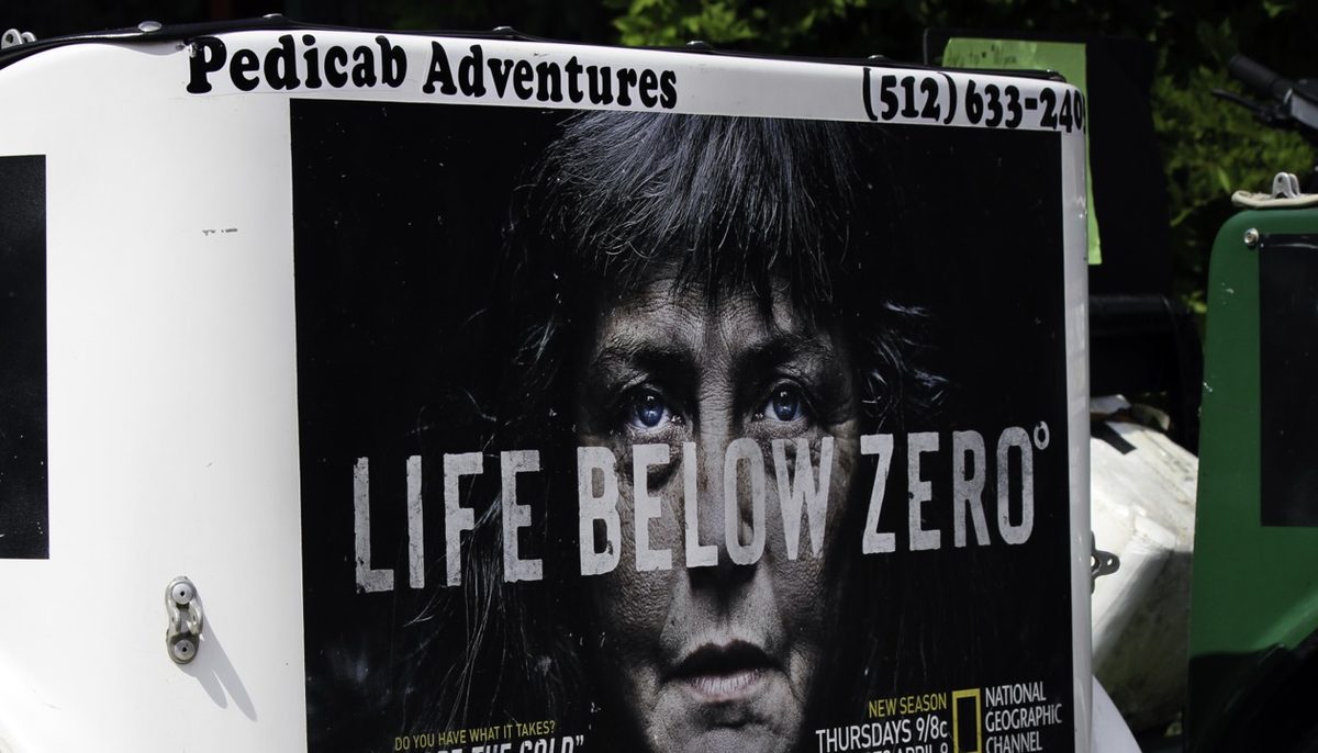 Close-up of a Pedicab Adventures carriage carrying National Geographic's Life Below Zero campaign, with the company name and phone number lettered along the top edge