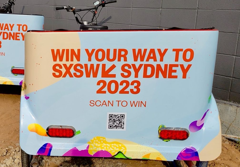 The rear panel of a wrapped pedicab reading Win Your Way To SXSW Sydney 2023 with a scan-to-win QR code