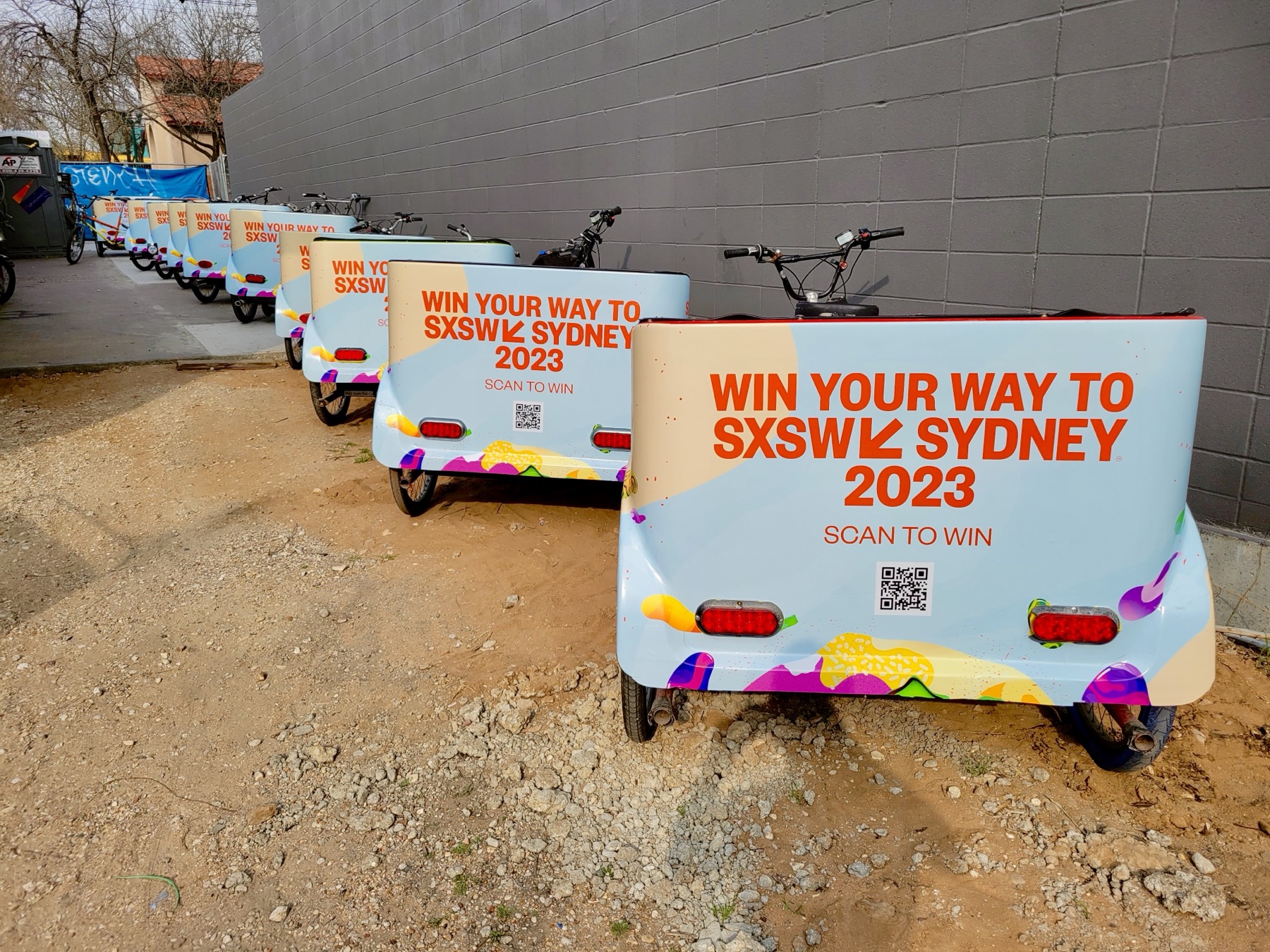 A row of pedicabs fully wrapped in a pastel SXSW Sydney 2023 campaign with scan-to-win QR codes on the back panels