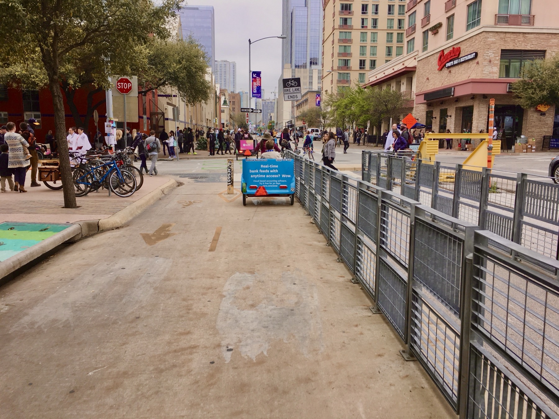 A Pedicab Adventures pedicab wrapped in a blue Xero advertising campaign riding down a barricaded downtown Austin street during SXSW